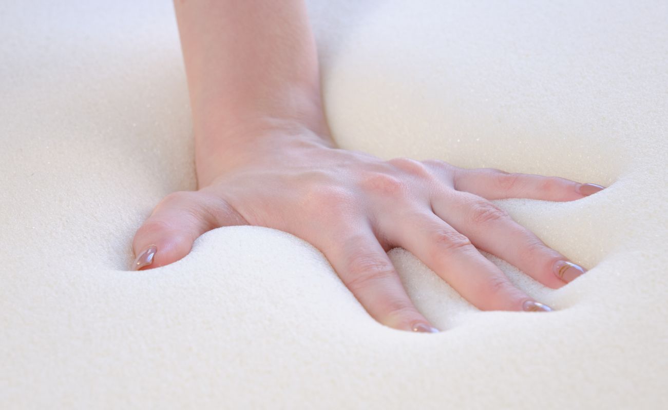 Eine Hand drückt in einen weichen, schaumstoffartigen Untergrund und hinterlässt eine Vertiefung.